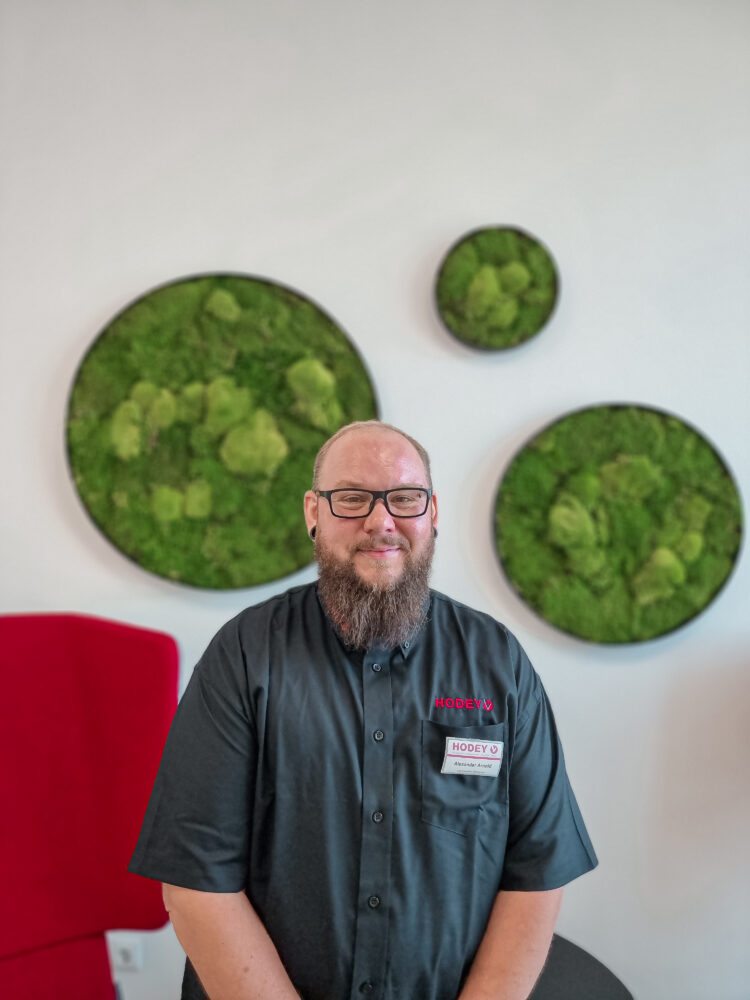 Alexander Arnold, Mitarbeiter von Hodey, vor einer grünen Mooswand, die Nachhaltigkeit symbolisiert.